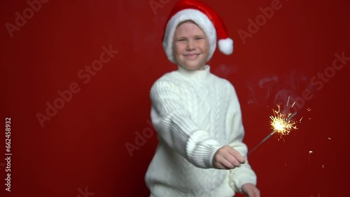 funny boy in Santa Claus cap holding sparkler on the red background. Concept Christmas