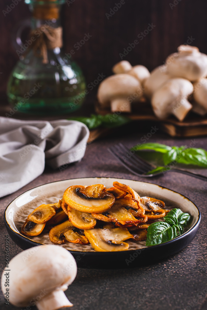 Appetizing fried champignons and basil leaves on a plate on the table vertical view