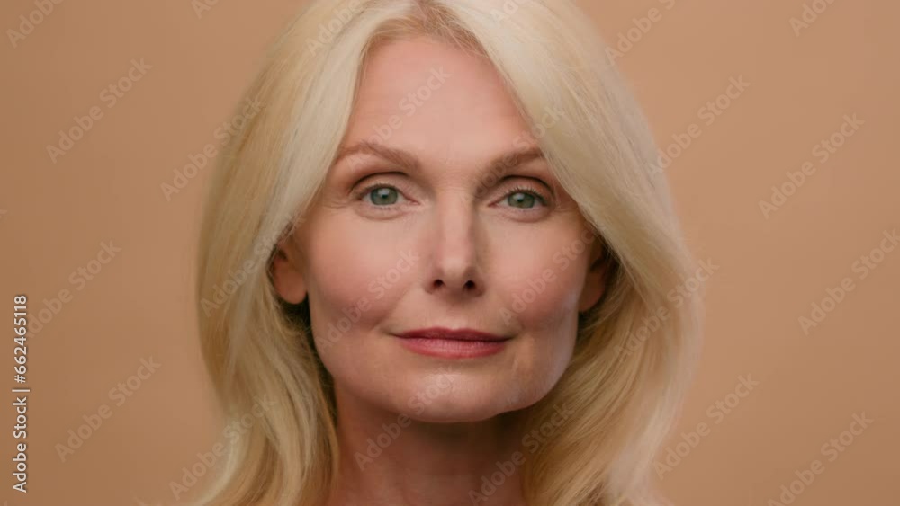 Beautiful mature middle-aged Caucasian woman close up face wrinkle skincare anti-aging lifting cosmetics moisturized skin beauty nude makeup senior lady looking to sides model casting in beige studio