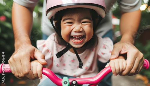 Close-up photo, a little girl wearing a slightly oversized helmet is being taught how to ride a bicycle by her father