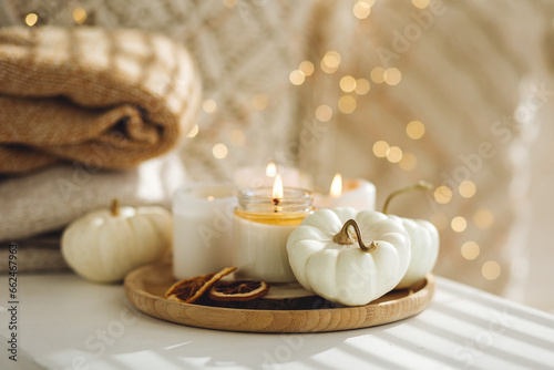 Atmospheric aroma candles with sweet spicy scent and white pumpkins on wooden tray, autumn bedroom decor. Autumn cozy home and hygge concept, place for relaxation, detention. Aromatherapy