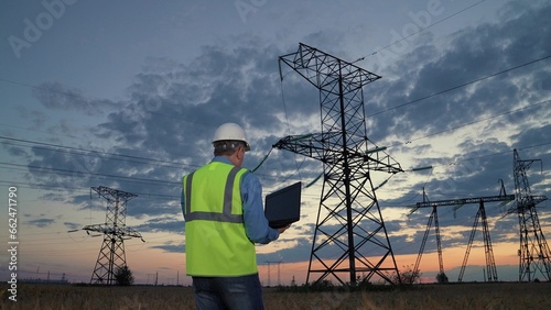 Engineer checks equipment with laptop walking to power transmission lines