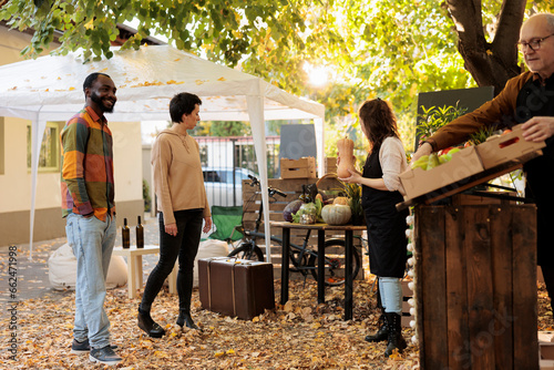 Young multiracial family couple visit farmers market to shop for healthy local food. Vendors standing near organic produce stand greeting first customers, offering locally grown fruits and veggies