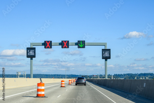 Overhead electronic highway sign, 2 left lanes closed, red x and green arrow, on a sunny blue sky day
 photo