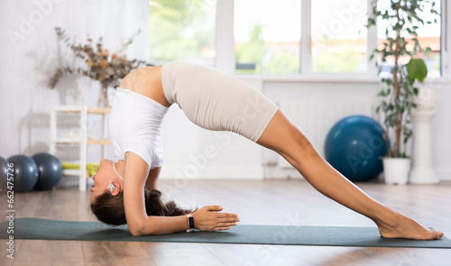 Skilled young female teacher demonstrating forearm stand pose of yoga in training room