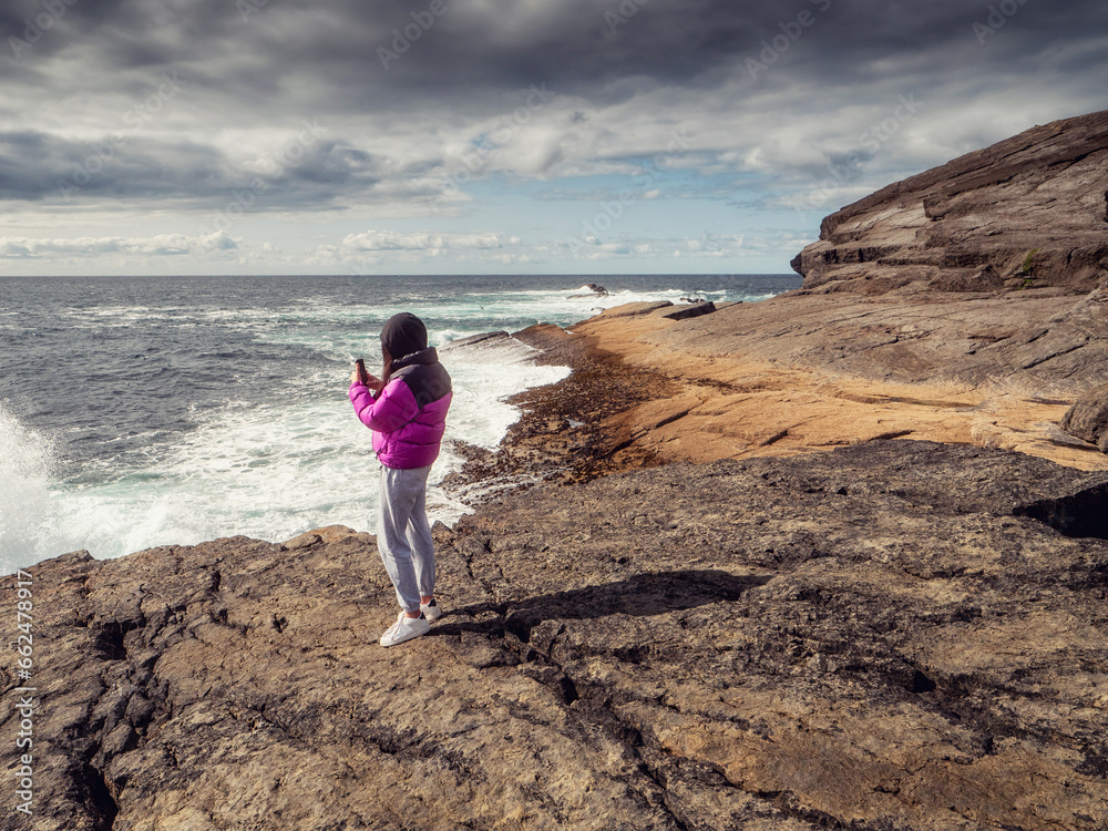 Young teenager blogger filming stunning nature scene on her smart phone. Ireland, Kilkee area. travel, tourism and sightseeing concept. Irish landscape and coastline. Influencer at work. Live show.