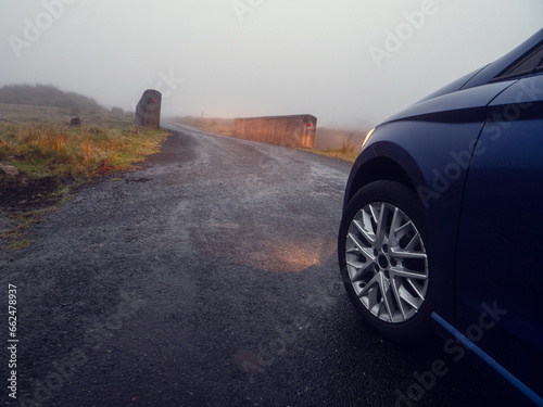 Car illuminating small narrow bridge in a country side, low visibility due to fog. Dangerous road situation because of state of the weather. Travel in rural area in mist and rain.