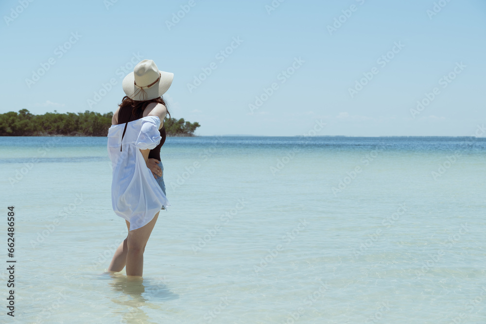 white woman standing on the shore of the beach looking at the horizo