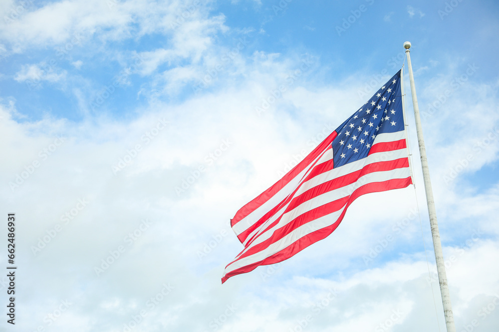 Fototapeta premium US flag waving in the wind against a blue sky. Symbol of freedom, unity, and national pride. Perfect for patriotic themes