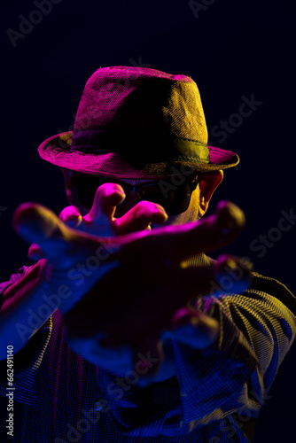 Portrait of a serious mysterious man with a beard wearing a hat and sunglasses making gestures with his hands.