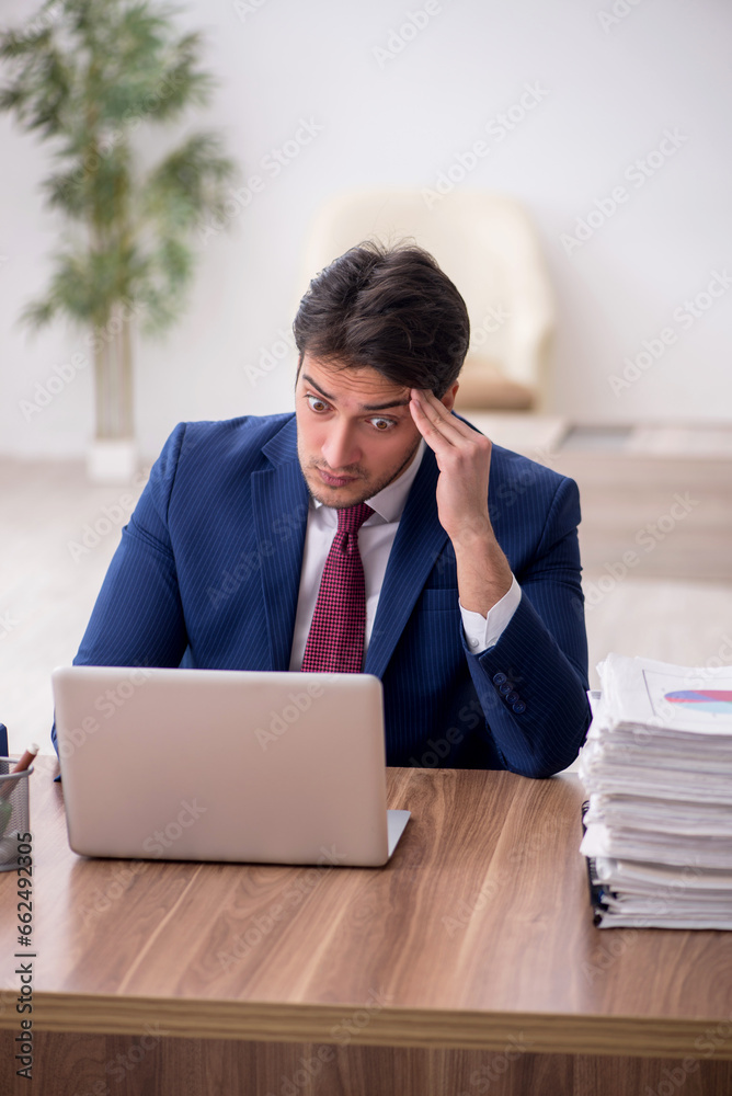 Young male employee unhappy with excessive work in the office Young male employee unhappy with excessive work in the office