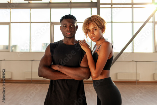 young sporty african american couple in sportswear stands with their arms crossed in the gym