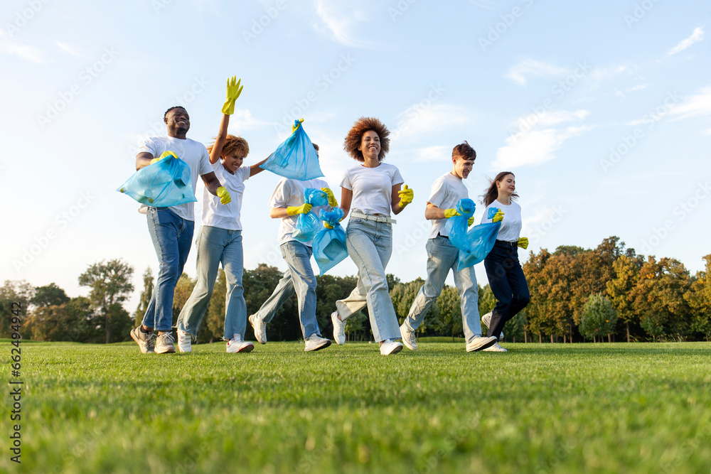 multiracial group of people running to clean the park from garbage and plastic with gloves and garbage bags