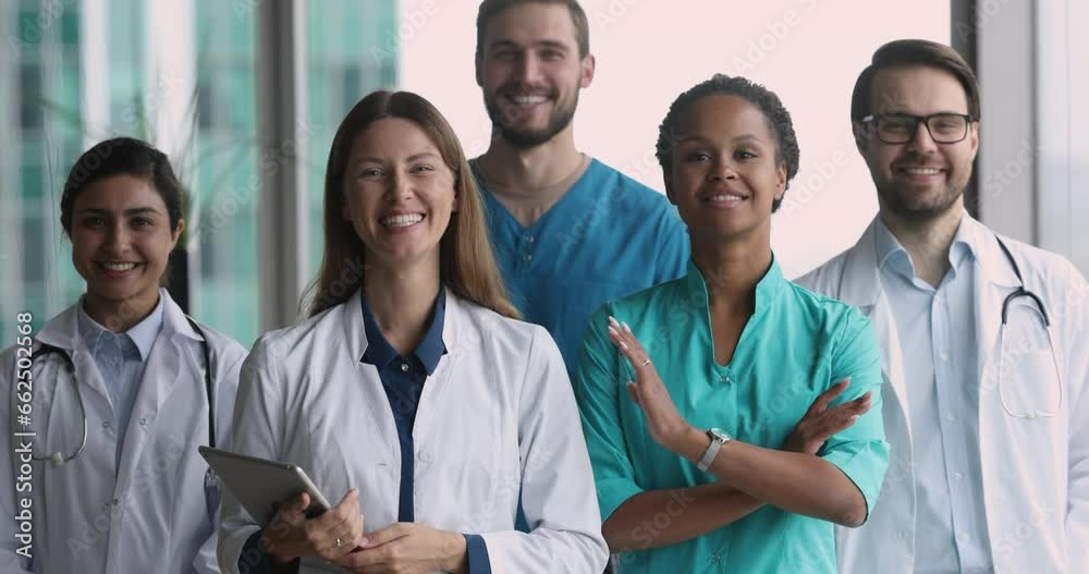 Group of confident millennial diverse doctors wear uniforms pose in clinic office. Hospital personnel team members smile look at camera standing indoors. Healthcare, medicine, professional occupation