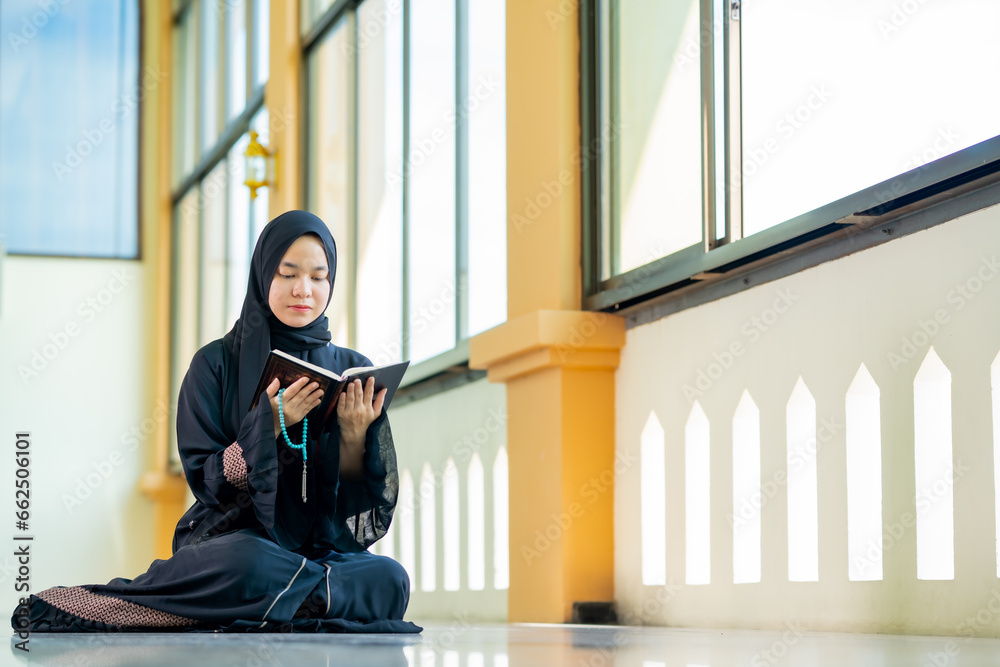 The image of an Asian Muslim woman in the Islamic religion in hijab in black color. reading the Quran and having a happy Staying in a beautiful mosque, Arabic word translation: The Holy Al Quran. The image of an Asian Muslim woman in the Islamic religion in hijab in black color. reading the Quran and having a happy Staying in a beautiful mosque, Arabic word translation: The Holy Al Quran.