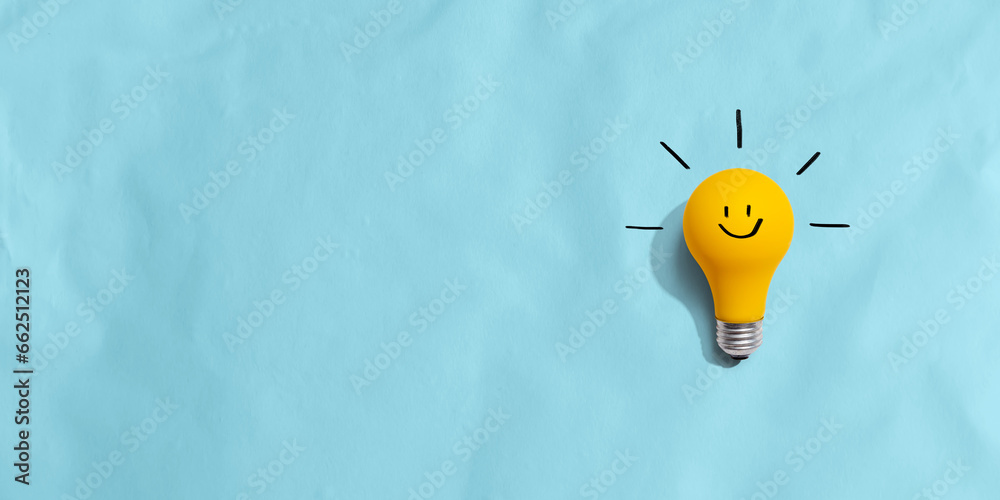 Yellow light bulb with happy face - flat lay - obrazy, fototapety, plakaty 