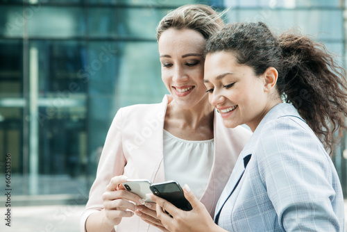 Two business women with mobile phone near office photo