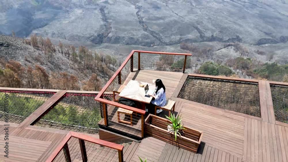 woman in glasses working with laptop on cafe balcony with view of Mount Bromo in Indonesia. outdoor working and remote working concept. woman in glasses working with laptop on cafe balcony with view of Mount Bromo in Indonesia. outdoor working and remote working concept.