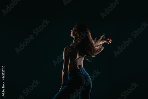 Female fitness model showcases transformed body in studio. Silhouette against dark background highlights muscular physique and defined abs. Perfect for fitness motivation and healthy lifestyle themes.