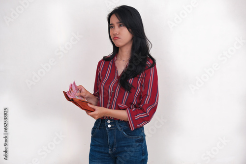 Facial expression of a young Indonesian woman counting money from her wallet photo
