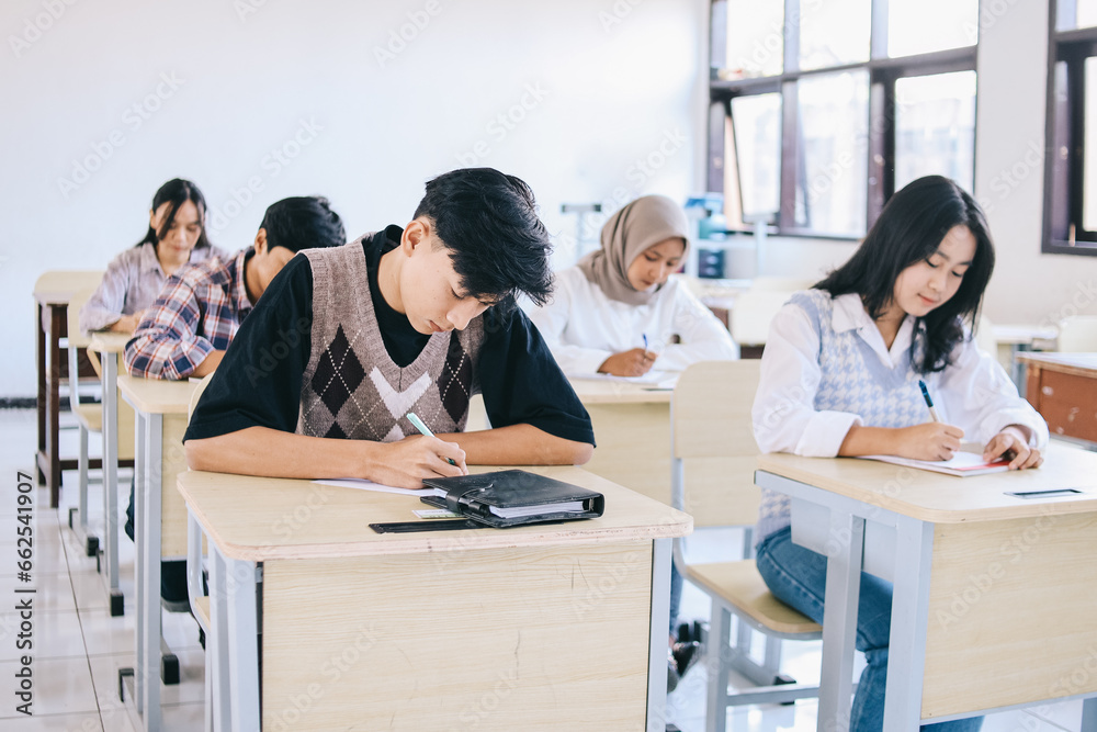 Group of high school students sitting in classroom and writing in notebooks.