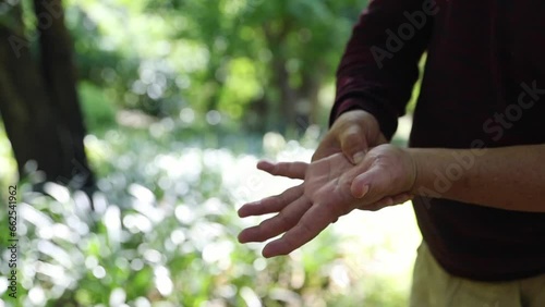 Elderly man stands and massages his palms and wrists, using his right hand to apply pressure points to relieve aches and pains from rheumatism. photo