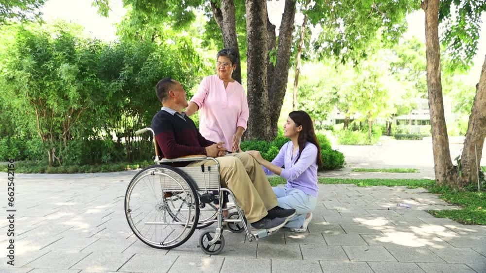 Family is warm the wife and daughter taking care father who is not in good health suffering parkinson's disease sitting wheelchair walking in the garden giving dad good mental health and peace mind.