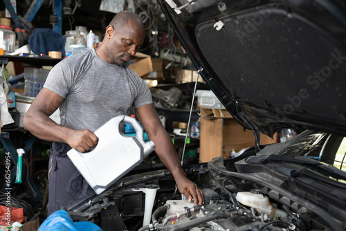 African mechanic worker filling engine oil into a car in garage