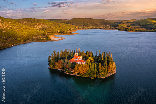 Visovac, Croatia - Aerial view of Visovac Christian monastery island in Krka National Park on a sunny autumn morning with golden sunrise, colorful autumn foliage and clear turquoise blue water