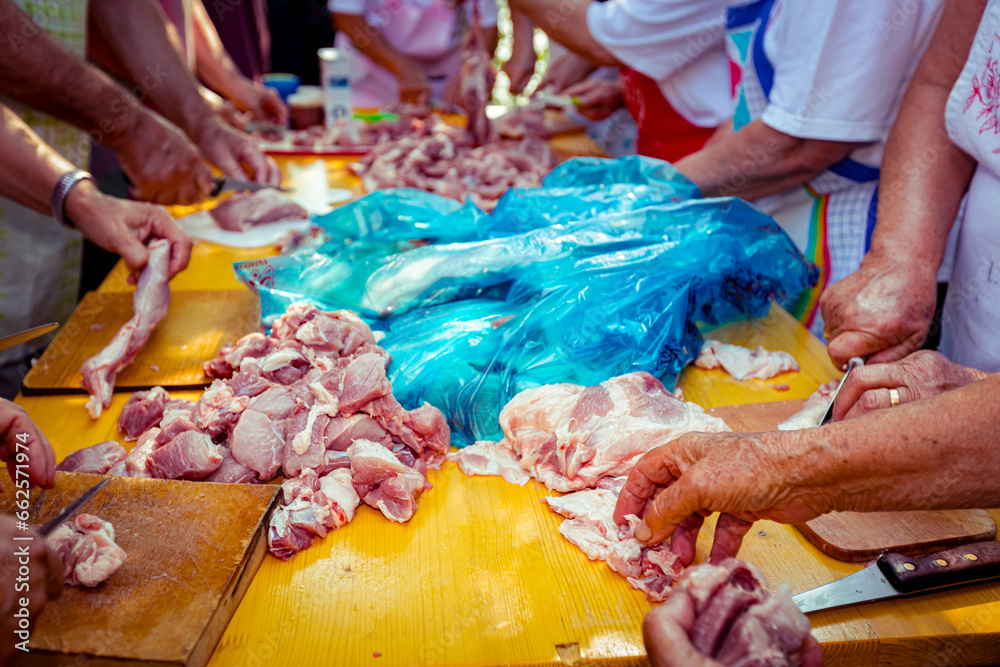 Elderly man and several women are cutting are cutting meat