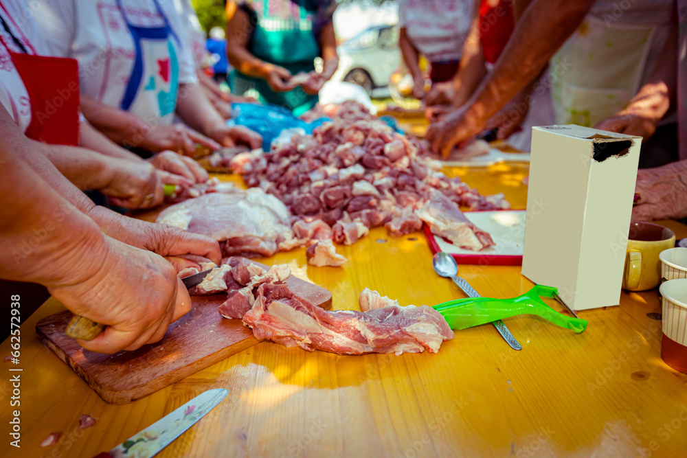 Elderly man and several women are cutting are cutting meat