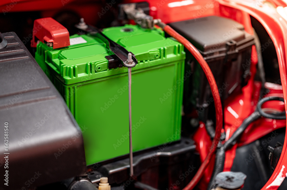 New green car battery installed near the car engine under the hood of red car in auto repair garage. Mechanical engineering and automotive industry concepts New green car battery installed near the car engine under the hood of red car in auto repair garage. Mechanical engineering and automotive industry concepts