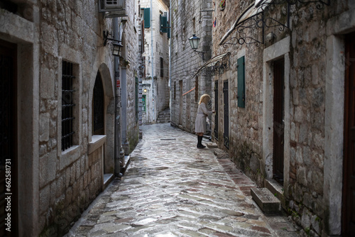 Montenegro, Sep 15, 2023: A blonde woman wearing a raincoat leaves home in Kotor Old Town © DeStefano