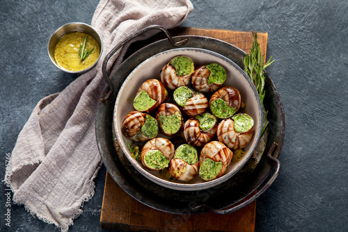 Snails with herbs butter,  French traditional food with parsley and bread on grey background.