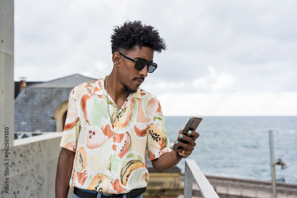 Stylish african american man using phone next to the sea
