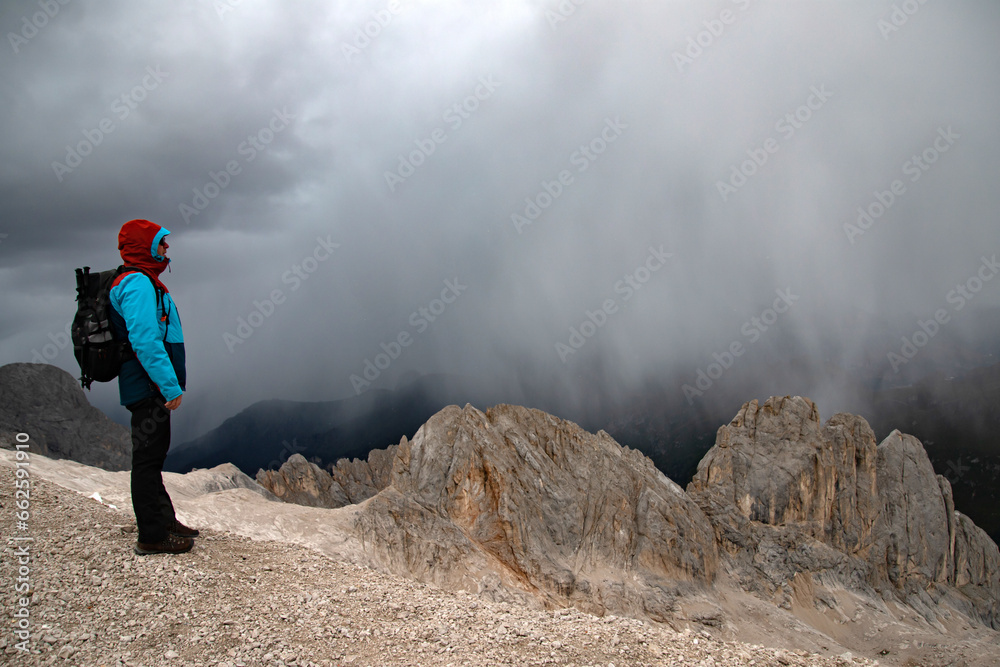 Young man hiking in the Dolomites (Italy) on Marmolada mountain, on a stormy summer day.