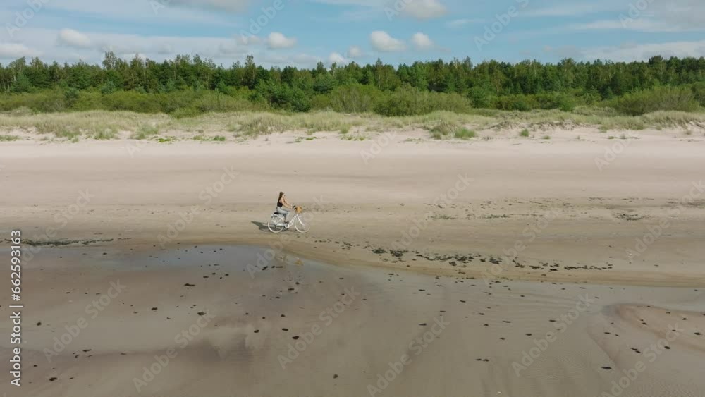 Aerial view with a young longhaired girl riding a bike on the sandy beach, sunny day, white sand beach, active lifestyle concept, wide drone dolly shot moving right, slow zoom in