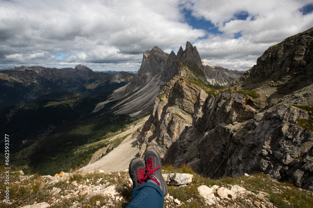 Trekking boots of a hiker while sitting on top of a mountain in Seceda, Dolomites, Italy