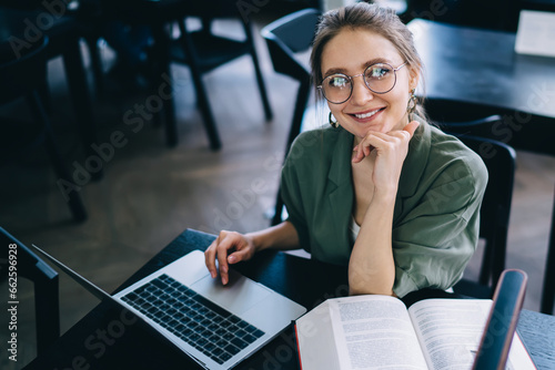 Smiling woman sitting at laptop and looking at camera while studying photo