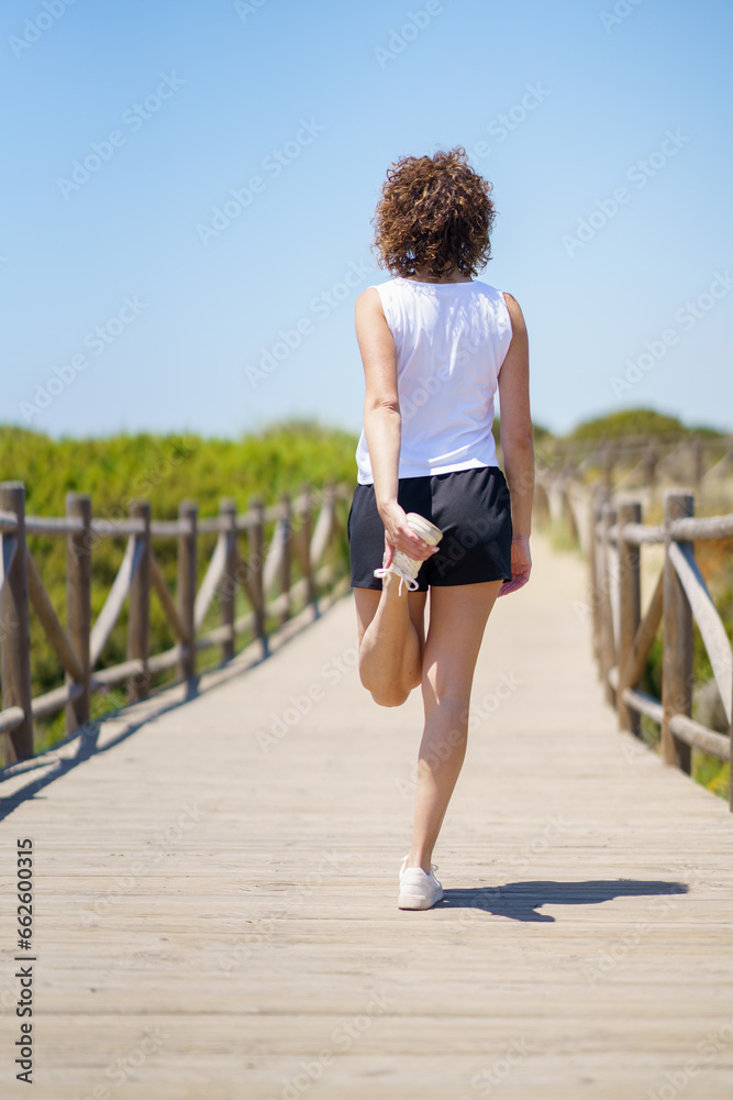 Unrecognizable fit woman stretching leg on boardwalk