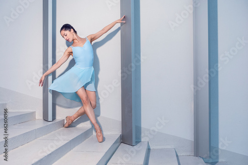 Graceful Sexy Slim Professional Caucasian Ballet Dancer in Blue Tutu Dreass Whie Posing Against White Wall In Dance Pose On Stairs In Stretching Outdoor.