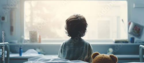 Obraz na plátně Frightened boy holding teddy bear with IV sitting on hospital bed looking out wi
