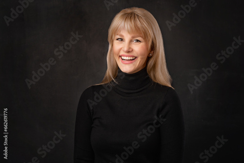 Confident blond haired woman wearing black turtleneck sweater against dark background