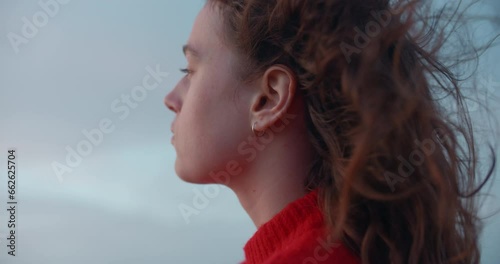 Portrait of young beautiful woman look pensive into distance. Strong ocean breeze or sea wind blow her hair. Free and youthful new generation. Cinematic real people, empowered woman 