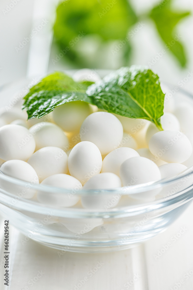 Mint candies in bowl. Menthol bonbons and mint leaves on white table. Mint candies in bowl. Menthol bonbons and mint leaves on white table.