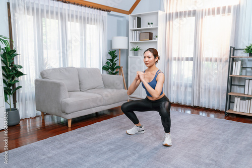 Vigorous energetic woman doing exercise at home. Young athletic asian woman strength and endurance training session as home workout routine with squat.