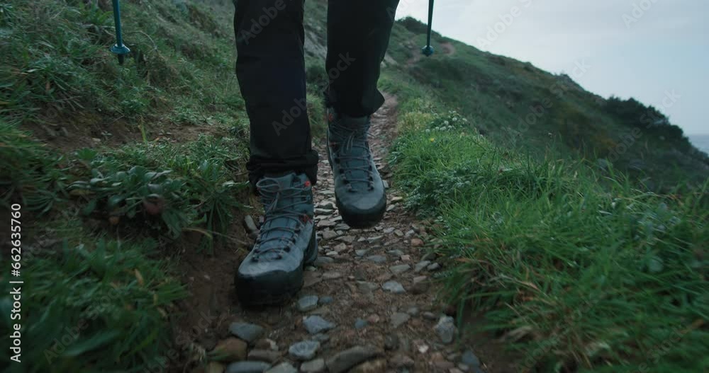 Gimbal stabilized shot of person feet in hiking waterproof boots on laces walk on secluded mountain trail. Hiking in epic scenery, green rocky path. Inspiring adventure lifestyle,backpacking in nature Gimbal stabilized shot of person feet in hiking waterproof boots on laces walk on secluded mountain trail. Hiking in epic scenery, green rocky path. Inspiring adventure lifestyle,backpacking in nature