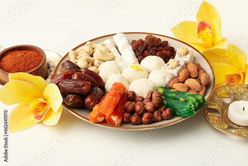 Plate with sweets, candle, flowers and spices on white background