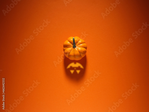 Halloween concept. Pumpkin with spooky Jack O lantern face shadow over orange colored background. photo