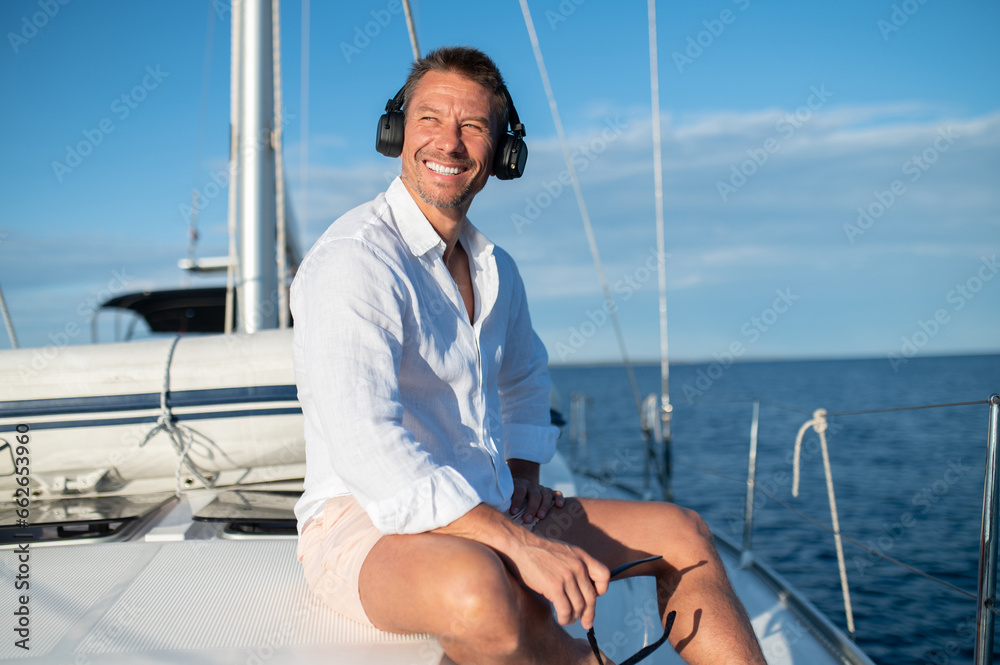 Happy man in headphones listening to music while sailing on a yacht